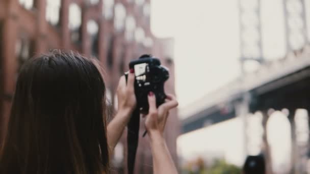 Atrás vista feliz turista femenina con cámara toma fotos del puente de Brooklyn desde el mirador Dumbo, Nueva York, se aleja 4K — Vídeo de stock