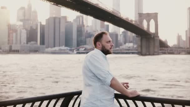 Homem de negócios europeu feliz fica perto de cerca de aterro rio em Brooklyn Bridge New York, olhando para relógio inteligente 4K . — Vídeo de Stock