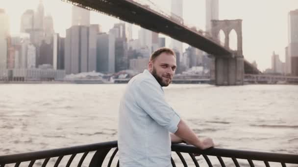 Retrato de plano medio del exitoso empresario independiente caucásico sonriendo a la cámara cerca del terraplén del puente de Brooklyn 4K . — Vídeo de stock