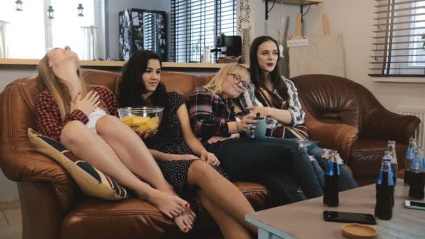 Las amigas se sientan en el sofá, ven telenovela en la tele. Jóvenes hermosas chicas disfrutando de la comedia romántica cámara lenta 4K . — Vídeo de stock