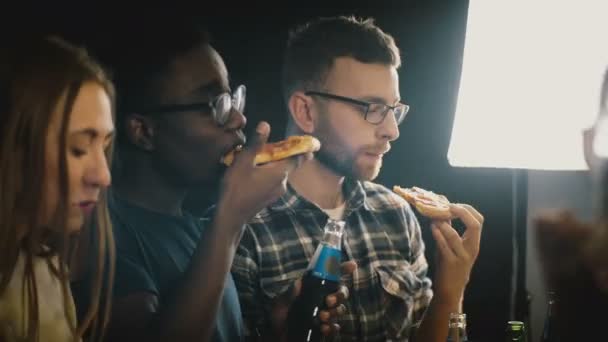 Multietnisk grupp unga människor njuta av pizza och drinkar i en avslappnad hus parti. Vänner äta snabbmat och dans. — Stockvideo