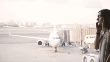 Genç Avrupalı kadın üzgün ve uçuş eksik sonra hayal kırıklığına Havaalanı terminal penceresi yakınındaki telefonda söz.
