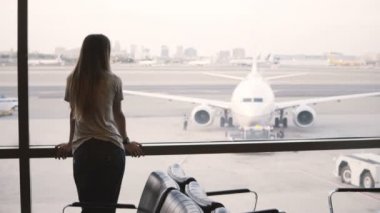 Genç Avrupa işkadını Havaalanı terminal Salon penceresinden bakarak duruyor, bakar ve akıllı izle kullanır.