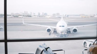 Avrupa kadın turist Havaalanı lounge terminal penceresine yürür, çantasını koyar ve geçen uçakları izlememiz görünüyor.