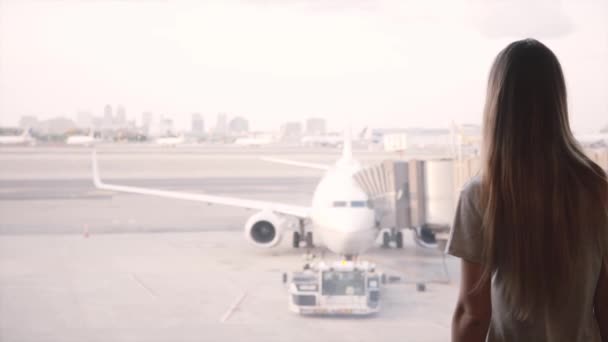 Hermosa viajera femenina camina hasta la ventana de la terminal del salón del aeropuerto para pararse y disfrutar de la vista de los aviones que pasan . — Vídeo de stock