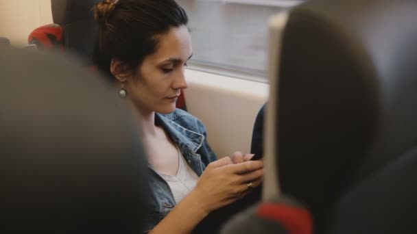 Casual vrouwelijke passagier in de trein zit in een comfortabele stoel met behulp van smartphone e-commerce app, kijken naar het venster. — Stockvideo