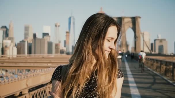 Όμορφο κορίτσι Καυκάσιος απολαμβάνοντας ζεστή ηλιόλουστη καιρικές συνθήκες, γυρίζοντας το κεφάλι και βλέπει κάμερα χαμογελώντας στη γέφυρα του Μπρούκλιν 4k. — Αρχείο Βίντεο