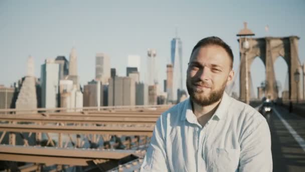 Портрет успешного кавказского бизнесмена, скрещивающего оружие, улыбающегося перед камерой на Бруклинском мосту, Нью-Йорк 4К — стоковое видео