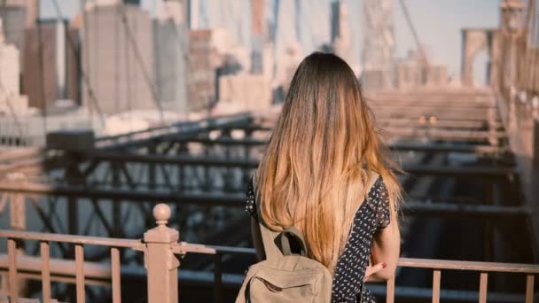 Jonge vrouwelijke blanke toerist in stijlvolle zonnebril met rugzak staan in Brooklyn Bridge, New York City, 4k. — Stockvideo