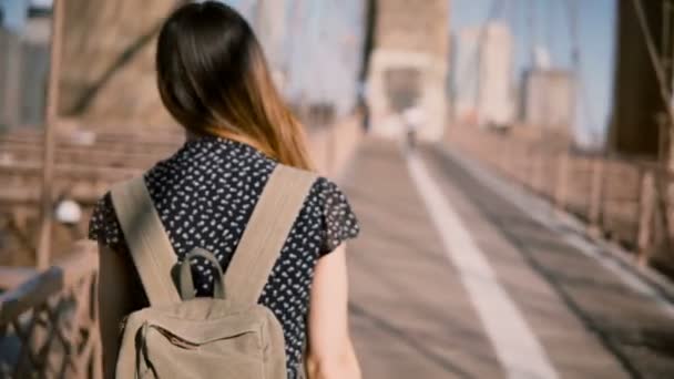 Kamera mengikuti turis wanita dengan ransel dan rambut emas gelap yang berjalan di sepanjang Jembatan Brooklyn pada hari yang cerah dan cerah 4K . — Stok Video