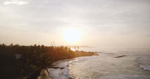 Drohne fliegt vorwärts über schönen Sonnenuntergangsstrand, weiße Meereswellen erreichen Küstenlinie mit laufender Baustelle. — Stockvideo