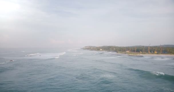 Drone aéreo tiro de belas ondas marinhas espumantes atingindo a costa tropical com árvores verdes, casas e canteiros de obras . — Vídeo de Stock