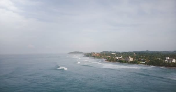 Aerial drone flyover shot of idyllic foaming ocean waves reaching magnificent tropical resort shore with buildings. — Stock Video