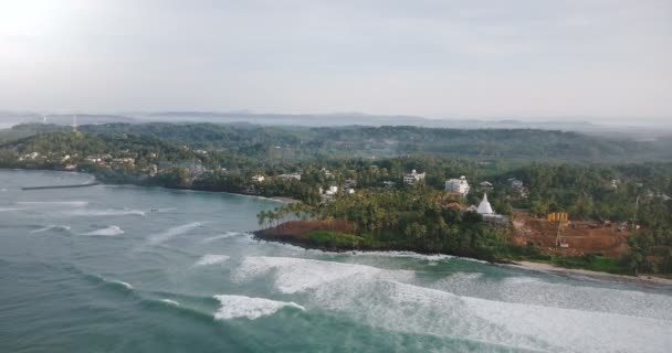 Drone pannen recht boven de geweldige exotische tropisch strand, seafoam golven, gebouwen onder bomen en bouwplaats. — Stockvideo