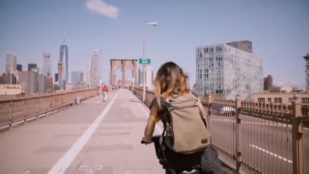 Bakifrån kvinna med mörkt hår som blåser i vinden cyklar längs en vacker cykel körfält på Brooklyn Bridge, Nyc. — Stockvideo