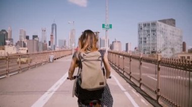 Arkadan Görünüş kadın serbest işçi uzun uçan saç zevk hafta sonu bisiklet ile binmek Brooklyn köprüsünde, ağır çekim.