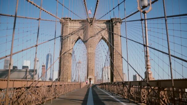 Young European romantic couple spin holding each other, run to camera holding hands at Brooklyn Bridge on a summer day. — Stock Video