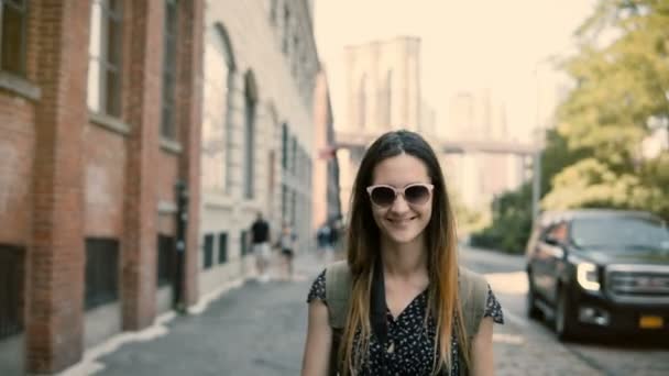 Camera follows happy excited European tourist girl with backpack and camera in sunglasses smiling, turning around 4K. — Stock Video
