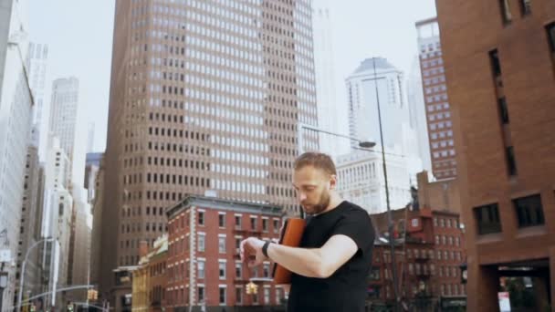 Jeune homme d'affaires beau tenant des documents, regardant la montre et marchant dans le quartier financier, New York. Mouvement lent . — Video