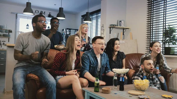 Multi-ethnic happy sports fans celebrate goal. 4K slow motion. African American friends support favourite team on TV.