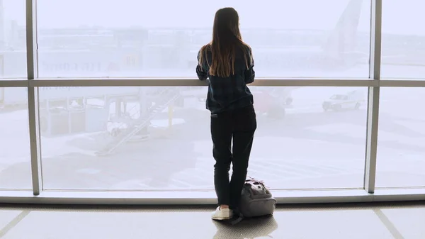 Mujer con mochila camina a la ventana del aeropuerto. Feliz chica europea exitosa de pasajeros con teléfono inteligente en la terminal. 4K . —  Fotos de Stock