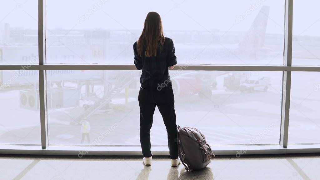Young woman with backpack near terminal window. Caucasian female tourist using smartphone in airport lounge. Travel. 4K.