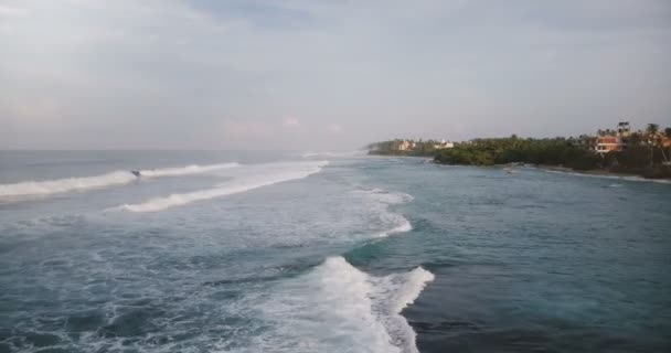 Εναέριο κηφήνα shot καταπληκτική αφρίζοντας ωκεανό κύματα φτάνοντας και σπάσιμο στην ακτή τροπικό θέρετρο με ξενοδοχεία και σπίτια. — Αρχείο Βίντεο