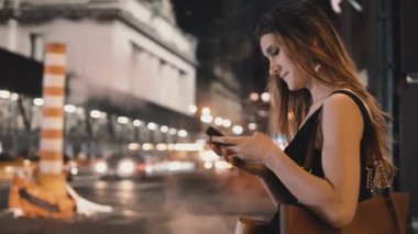 Şehir merkezinde akşam ve New York, Amerika smartphone kullanarak duran genç güzel kadın.