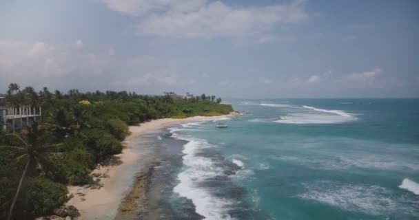 Drone viaduct schot van exotische resort strand met kleine boot, tropische bomen, schuimende golven over mooie oever. — Stockvideo