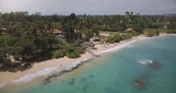 Drone voando em torno de pequena casa idílica resort oceano com palmeiras, ondas lavar a costa com água azul claro . — Vídeo de Stock