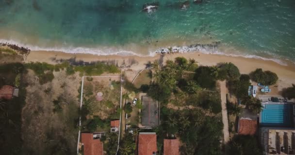 Зафіксувати повітряний постріл екзотичного узбережжя океану курортні будинки з пальмами, хвилі миття прекрасного пляжу в сонячний день . — стокове відео