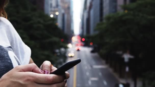 Detailní pohled ženských rukou držení a používání smartphone, stojící na mostě v New Yorku, Amerika. — Stock video