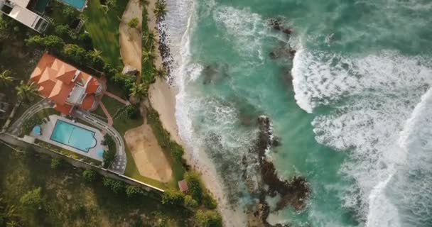 Flyover drone aéreo tiro de litoral oceano idílico, espumando ondas brancas atingindo exóticas casas de praia resort tropical . — Vídeo de Stock