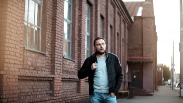 Retrato de plano medio del hombre europeo casual. Hombre joven y relajado en chaqueta de cuero está esperando. Edificio de ladrillo rojo 4K . — Vídeo de stock