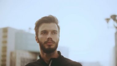 4k ileriye düşünceli adam portresi. Sakallı Kafkas yakışıklı erkek güneş ışığı parlama modern şehir arka planda.