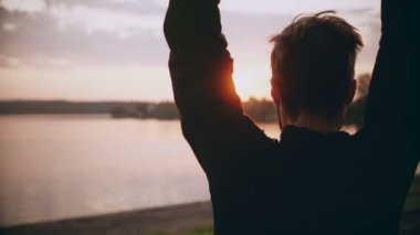 4 k sportif adam sessiz sunset nehir kenarında ısınıyor. Silah sallanan ve güzel nehir panorama atlama arkadan görünüm.