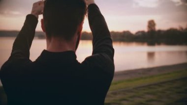 4 k genç adam germe silah bir gündoğumu lake yakınındaki. Arkadan görünüm. Erkek sporcu güzel hala görünümü ısınma uygun.