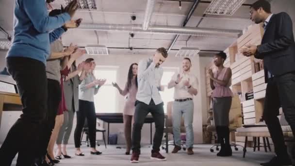 Joven empleado caucásico bailando con sus colegas, celebrando el logro de negocios en la fiesta de oficina casual cámara lenta . — Vídeos de Stock