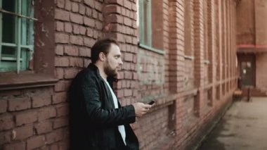 Mutlu başarılı rahat Avrupa adam akıllı telefon sosyal app dışında ve gülümseyerek, kırmızı tuğla duvar arka planda kullanarak.