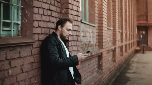 Happy successful Caucasian businessman using smartphone messenger app outside smiling near brick wall, then walking away — Stock Video