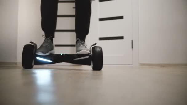 Närbild låg vinkel skott av manliga ben i sneakers flytta runt på gyro scooter i Lägenhet med vita väggar och dörrar — Stockvideo