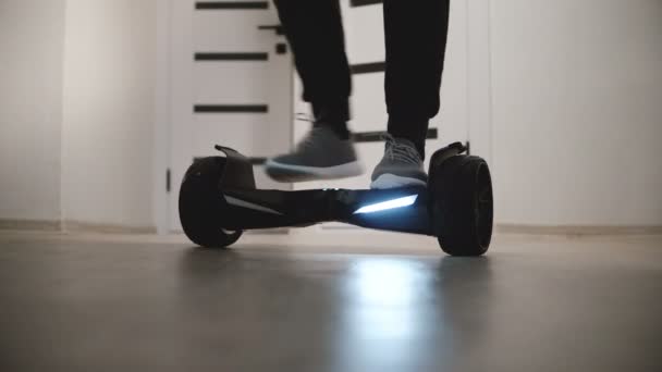 Nahaufnahme männlicher Beine, die sich auf einem Elektro-Gyro-Roller in einer Wohnung mit weißen Wänden bewegen und dann davonlaufen. — Stockvideo