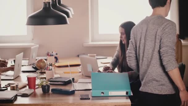 Мультиэтнические занятые молодые офисные работники сотрудничают за столом в оживленном коворкинге, люди ходят вокруг замедленной съемки . — стоковое видео
