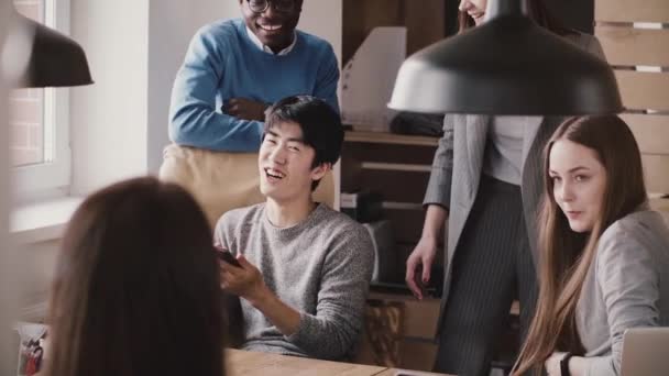 Szczęśliwy azjatycki biznes biznesmen oglądania wideo na smartphone z kolegami wieloetnicznym w nowoczesnym biurze, śmiejąc się w zwolnionym tempie. — Wideo stockowe