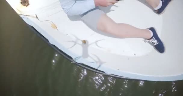 Vista superior del hombre europeo feliz que opera el dron con la cámara sentada en un pequeño barco del río, tomándolo y sosteniéndolo . — Vídeo de stock