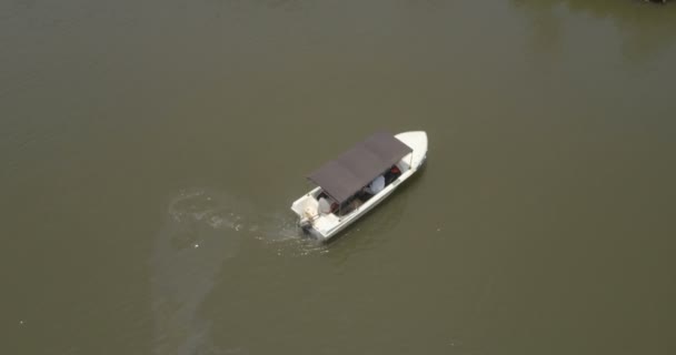 Blick von oben auf ein kleines weißes Safariboot, das inmitten eines großen, ruhigen, grünen Dschungel-Flusses dreht. — Stockvideo