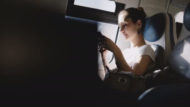 Belle fille caucasienne souriant, faire un appel téléphonique et regarder autour de voyager seul sur le siège de fenêtre de train moderne . — Video