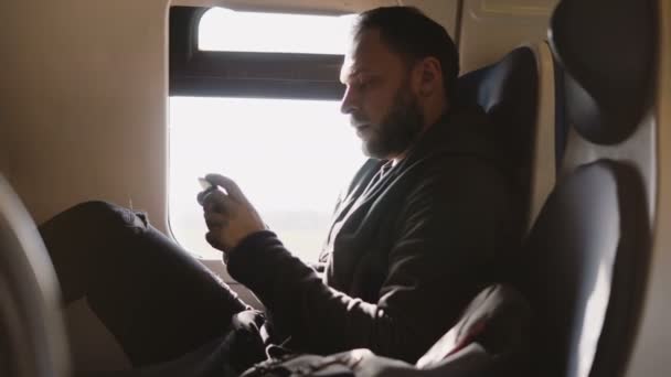 Confident successful Caucasian businessman using smartphone mobile office app while traveling on the train window seat. — Stock Video