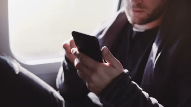 기차 창이 자리에 여행 하는 동안 스마트폰 애플 리 케이 션에 온라인 쇼핑 하는 편안 하 게 웃는 백인 남자의 클로 우즈 업 보기. — 비디오