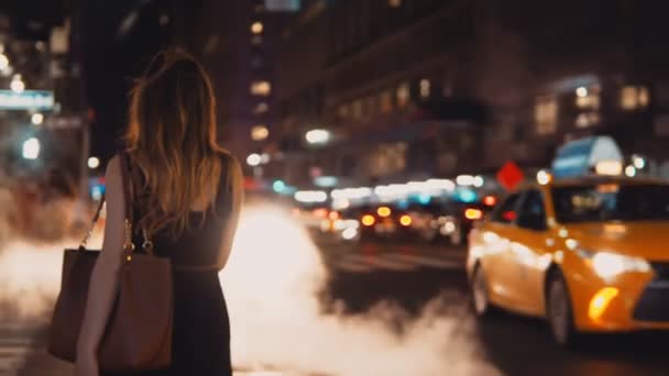 Achteraanzicht van jonge mooie vrouw staande op de weg van het verkeer in de avond, centrum van New York, Amerika. — Stockvideo